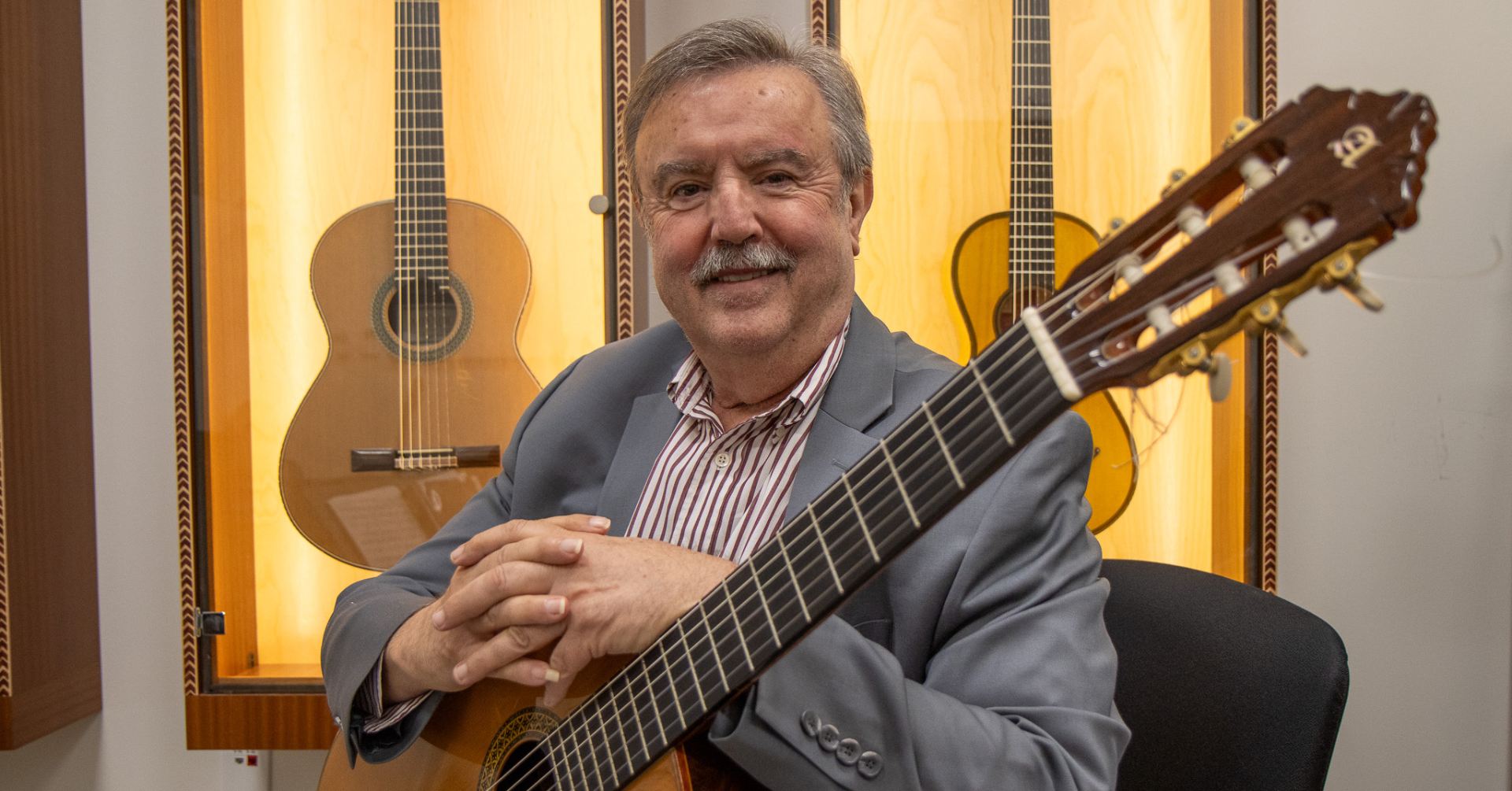 Dr. Enric Madriguera posing for a picture while holding a guitar in the PHY Bldg. in Aug. 2023.