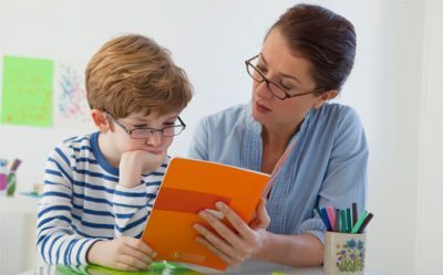 A woman reading a book to a young boy.